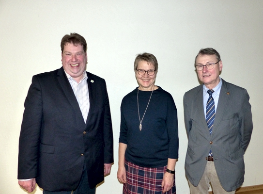 Eine Frau steht zwischen zwei Männern vor einer weißen Wand.